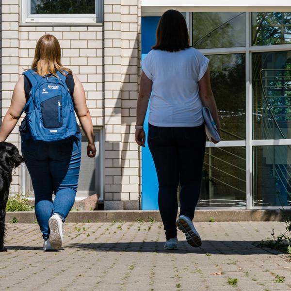 Zwei Mitarbeiterinne laufen mit ihrem Hund ins Bürogebäude