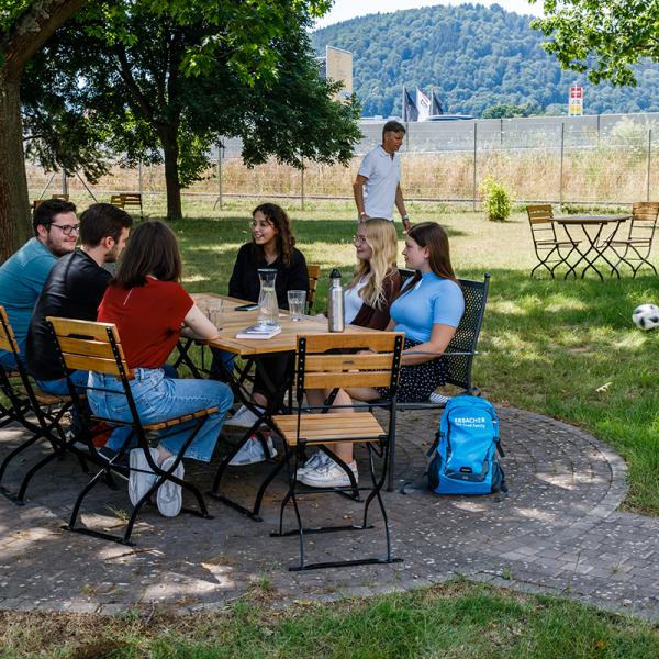 Viele Kollegen sitzen gemeinsam am Tisch im ff Park. Im Hintergrund wird auf dem Rasen Fußball gespielt.