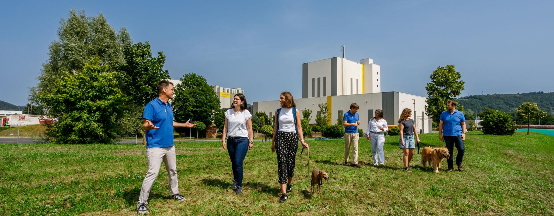 People walking in front of the company in Kleinheubach discussing while walking. Two of them also have a dog on the leash.